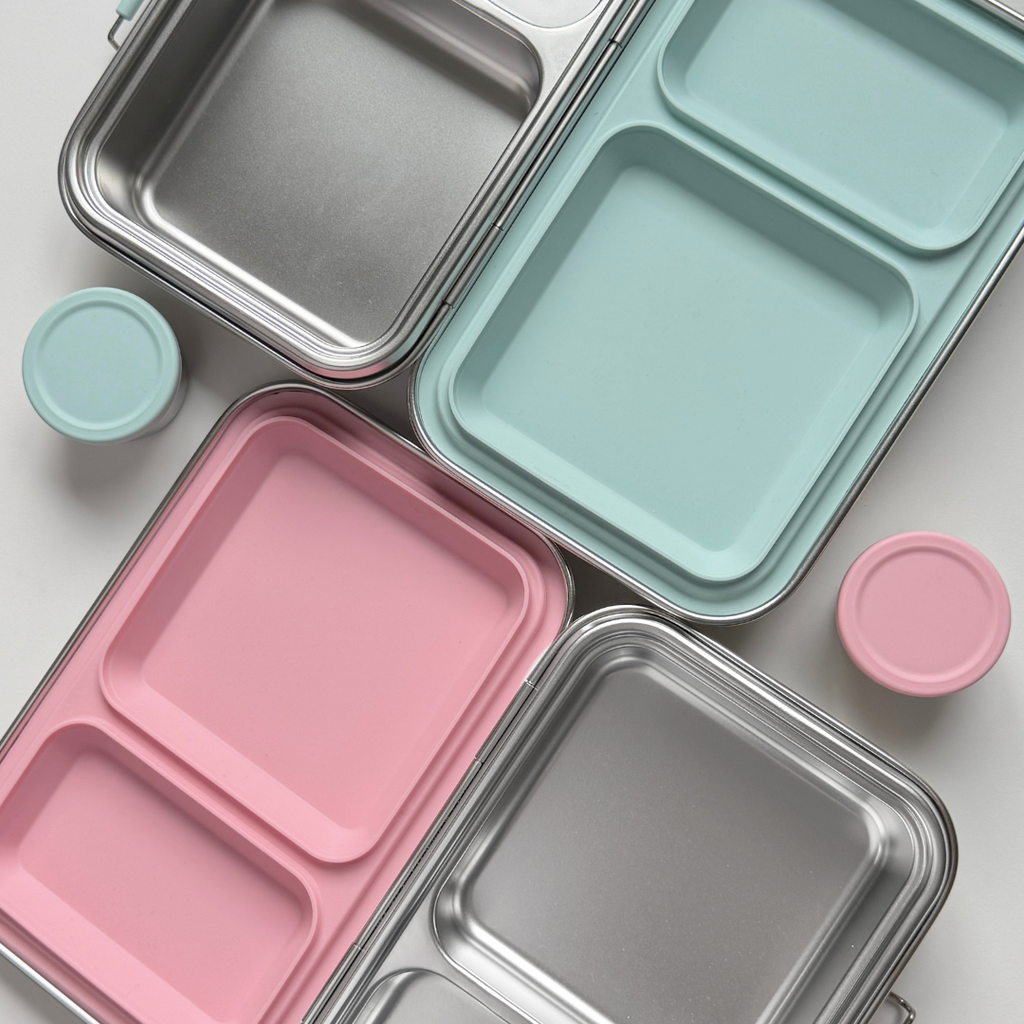 Close-up of stainless steel bento lunch box compartments with mint green and blush pink silicone inserts and sauce containers, modern minimal design by nom