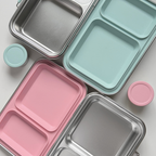Close-up of stainless steel bento lunch box compartments with mint green and blush pink silicone inserts and sauce containers, modern minimal design by nom