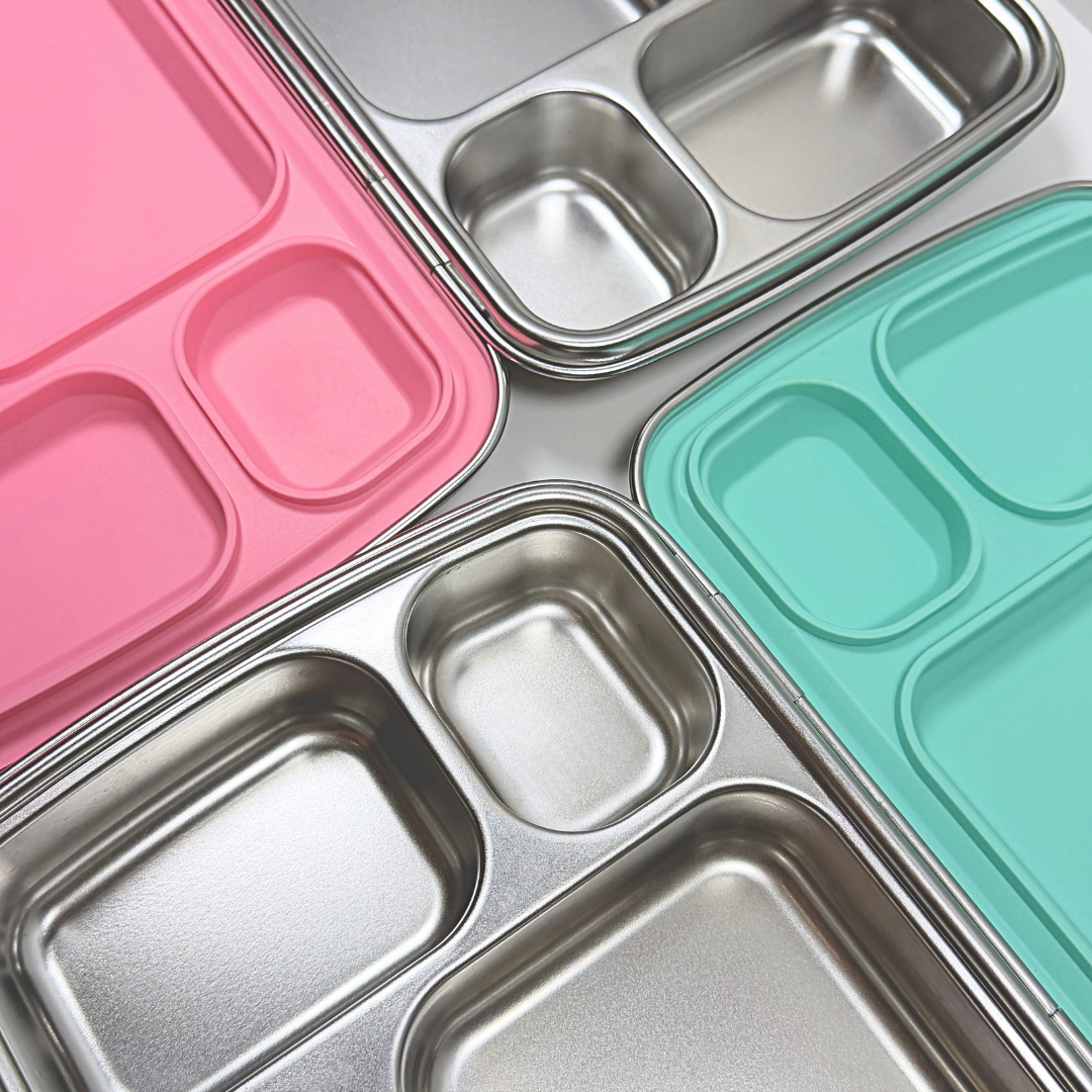 Close-up detail of stainless steel bento lunch box compartments with mint green and bubble gum pink silicone lids, nom quad